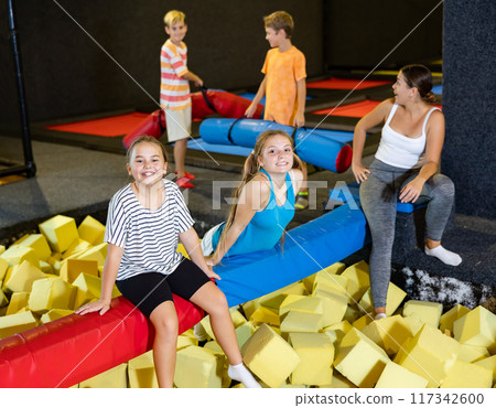 Happy tween girls sitting on soft beam above foam pit Happy tween girls sitting on soft beam above foam pit 117342600