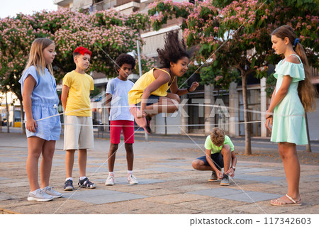 Cheerful preteen children playing chinese jump rope on city street Cheerful preteen children playing chinese jump rope on city street 117342603