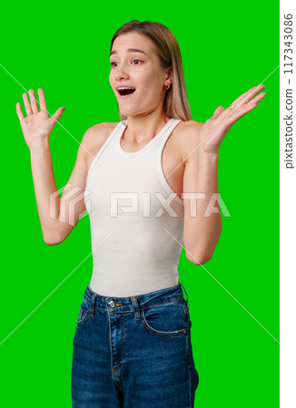 Young Woman With Blonde Hair Expressing Surprise With Open Mouth and Raised Hands Against Green Screen 117343086