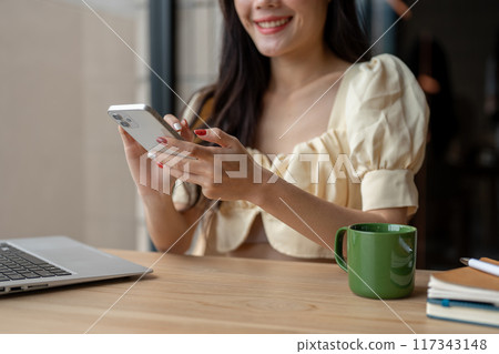 A cropped image of a woman checking messages or scrolling on her smartphone at a table indoors. 117343148