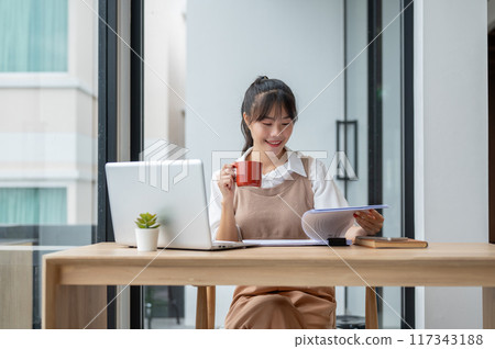 A beautiful Asian businesswoman is having her morning coffee while reviewing business paperwork. 117343188