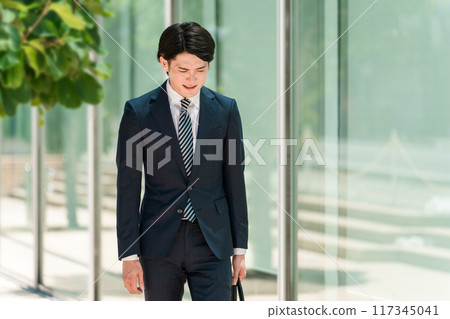 A young Asian male businessman in a suit walking with his head down (depressed, worried, troubled, laid off, distressed, anxious) A young Asian male businessman in a suit walking with his head down (depressed, worried, troubled, laid off, distressed, anxious) 117345041