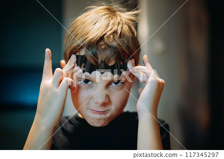 cute caucasian boy holding a paper bat shape on his forehead making scary face. 117345297