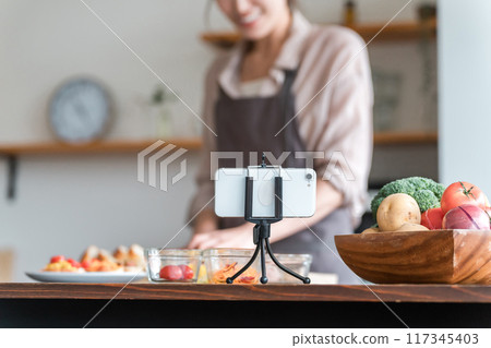 A housewife cooking in the kitchen while looking at a smartphone app A housewife cooking in the kitchen while looking at a smartphone app 117345403