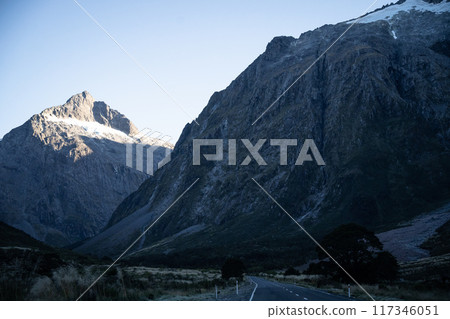 Empty highway leading through the valley with steep rocky walls in Fiordland, New Zealand 117346051