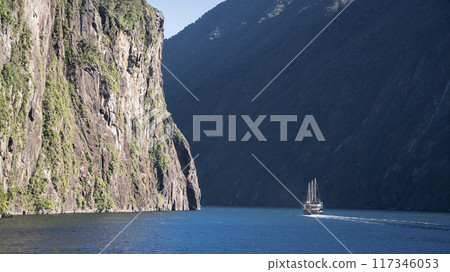 Tourist sightseeing boat sailing through fjord with steep rocky wall, Fiordland, New Zealand Tourist sightseeing boat sailing through fjord with steep rocky wall, Fiordland, New Zealand 117346053