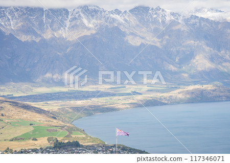 New Zealand flag waving above township with lake and big mountain range in backdrop 117346071