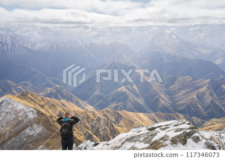 Female hiker standing on top of the mountain enjoying views on mountain ranges in front of her Female hiker standing on top of the mountain enjoying views on mountain ranges in front of her 117346073