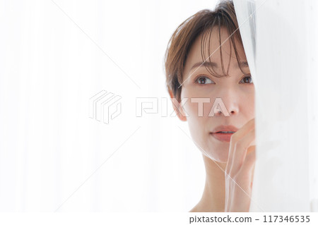 Middle-aged woman peeking through the curtains Middle-aged woman peeking through the curtains 117346535