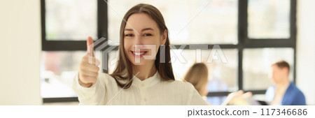 Smiling woman posing in office and showing thumb up sign 117346686