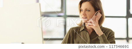 Smiling woman sitting on workplace and speaking by smartphone Smiling woman sitting on workplace and speaking by smartphone 117346691