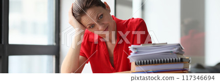 Overworked woman sitting at table littered with papers Overworked woman sitting at table littered with papers 117346694