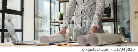 Designer standing near work desk with rolls of paper Designer standing near work desk with rolls of paper 117346820