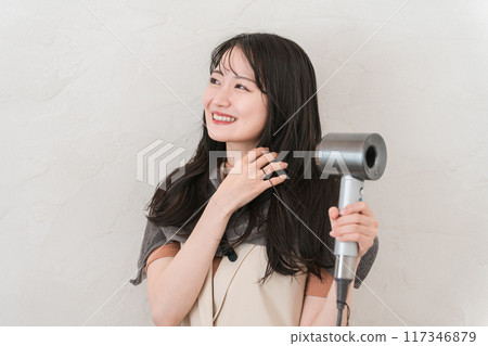 A woman blow-drying her hair with a hair dryer (hair care) 117346879