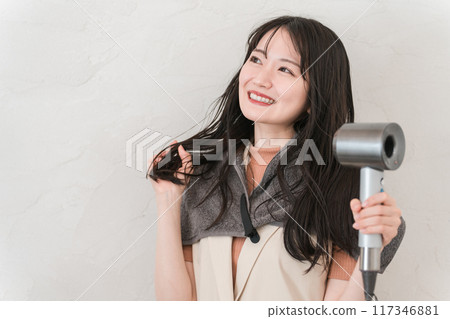 A woman blow-drying her hair with a hair dryer (hair care) 117346881