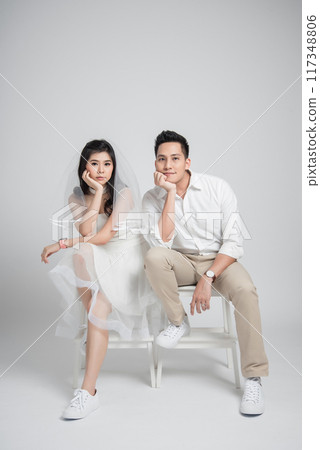 Happy young couple Asian groom and bride in casual wedding dress sitting on chair Happy young couple Asian groom and bride in casual wedding dress sitting on chair 117348806
