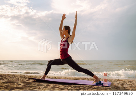 Yoga in the morning. Young woman in sportswear doing fitness exercise on beach. Healthy lifestyle. 117349650