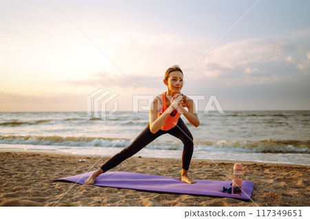 Yoga in the morning. Young woman in sportswear doing fitness exercise on beach. Healthy lifestyle. 117349651