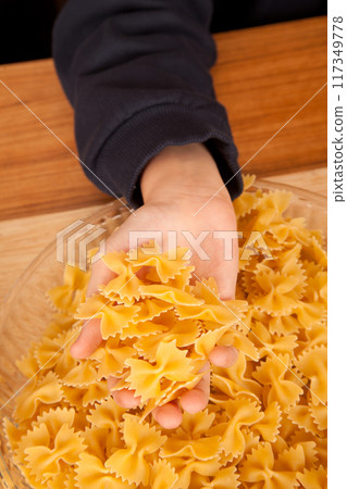 Uncooked raw healthy and pasta macaroni hand held by a Caucasian man, on wooden table in glass plate 117349778