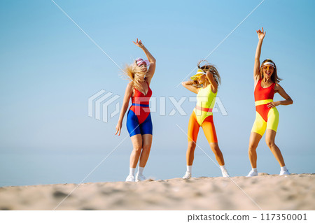 Three young woman - dancer dancing in bright swimsuits on the beach. Sport, fitness, active life. 117350001
