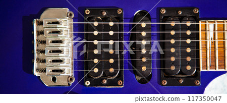 Electric guitar bridge, strings and pickup, detail close-up view of guitar pickup in wood paint blue Electric guitar bridge, strings and pickup, detail close-up view of guitar pickup in wood paint blue 117350047