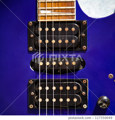 Electric guitar bridge, strings and pickup, detail close-up view of guitar pickup in wood paint blue Electric guitar bridge, strings and pickup, detail close-up view of guitar pickup in wood paint blue 117350049