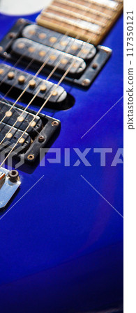 Electric guitar bridge, strings and pickup, detail close-up view of guitar pickup in wood paint blue Electric guitar bridge, strings and pickup, detail close-up view of guitar pickup in wood paint blue 117350121