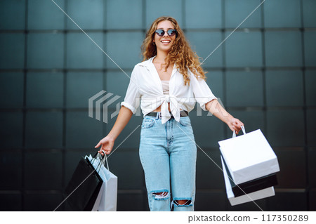 Young woman with shopping bags walking on street. Summer shopping. Sale, shopping, lifestyle concept 117350289