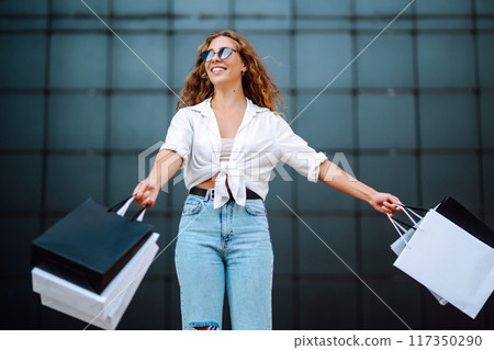 Happy stylish woman with shopping bags enjoys sunny weather walking down street. Summer shopping. Happy stylish woman with shopping bags enjoys sunny weather walking down street. Summer shopping. 117350290