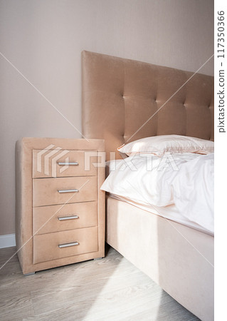 Beige dresser with four drawers near the bed. Well organized bedroom in natural light. Beige dresser with four drawers near the bed. Well organized bedroom in natural light. 117350366