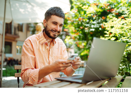 Man with laptop and phone sits in cafe and works. Business, blogging, freelance, education concept. 117351158