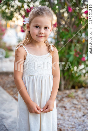 Portrait of little girl in white dress happy smiling on blooming park background in Croatia 117351216