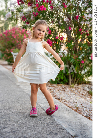 Portrait of little girl in white dress happy smiling and dancing on blooming park background in Croatia 117351217