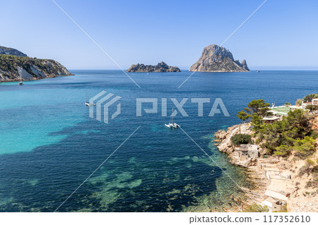 Overlooking Cala d'Hort in Ibiza, with clear blue waters, anchored sailboats, rocky shoreline Overlooking Cala d'Hort in Ibiza, with clear blue waters, anchored sailboats, rocky shoreline 117352610