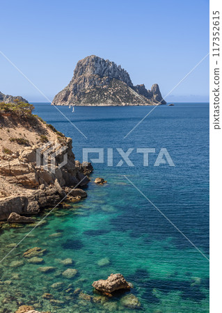 Vertical shot of Ibiza pristine waters and rugged cliffs with Es Vedra island in the background 117352615