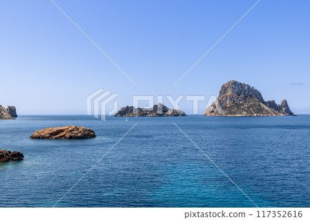 Es Vedra and Es Vedranell with sailboat on deep blue Mediterranean Es Vedra and Es Vedranell with sailboat on deep blue Mediterranean 117352616