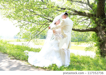Beautiful bride in wedding dress under fresh green cherry blossom tree Photo wedding Bride and groom location shoot Beautiful bride in wedding dress under fresh green cherry blossom tree Photo wedding Bride and groom location shoot 117352736