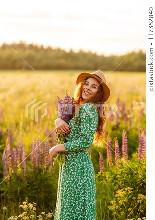 A beautiful woman with a bouquet of lupins, collects flowers, inhales fresh floral air. A beautiful woman with a bouquet of lupins, collects flowers, inhales fresh floral air. 117352840