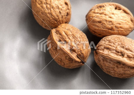 Unshelled whole rough walnuts in a kitchen ceramic plate with uneven rustic design. Organic nuts. Top view. Close up 117352960