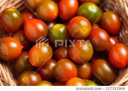 Fresh raw small kumato cherry tomatoes in a rattan bowl close up. Top view 117352964