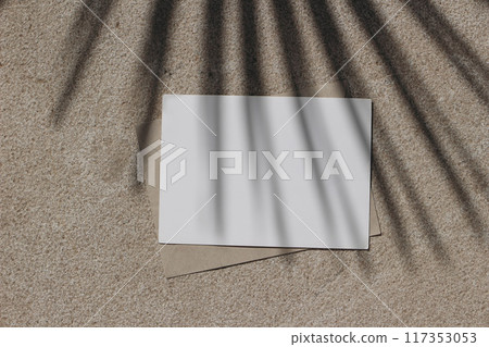 Empty horizontal greeting card invitation mockup, craft envelope. Beige limestone background in sunlight. Palm leaf shadow overlay. Modern branding template. Tropical summer, vacation. Flat lay, top Empty horizontal greeting card invitation mockup, craft envelope. Beige limestone background in sunlight. Palm leaf shadow overlay. Modern branding template. Tropical summer, vacation. Flat lay, top 117353053