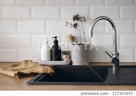Modern kitchen, Sacandinavian interior. Wooden countertop. Soap, detergent dispenser glass bottles mockup. Dish brush, black sink. Eco dish washing concept. White wall, metro tiles background 117353057