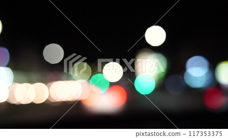 Blurred car lights bokeh in the evening city. Defocused headlights and street lighting at night. Moving bokeh circles of cars at night. Blurred city traffic background 117353375