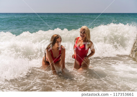 Women ocean play. Seaside, beach daytime, enjoying beach fun. Two women in red swimsuits enjoying themselves in the ocean waves. Women ocean play. Seaside, beach daytime, enjoying beach fun. Two women in red swimsuits enjoying themselves in the ocean waves. 117353661
