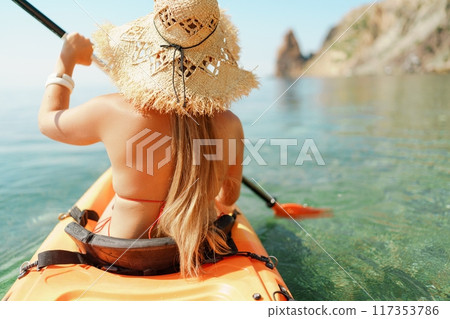 Woman in kayak back view. Happy woman with long hair in a swimsuit and hat floating in kayak on the sea. Summer holiday vacation. Summer holidays vacation at sea. 117353786