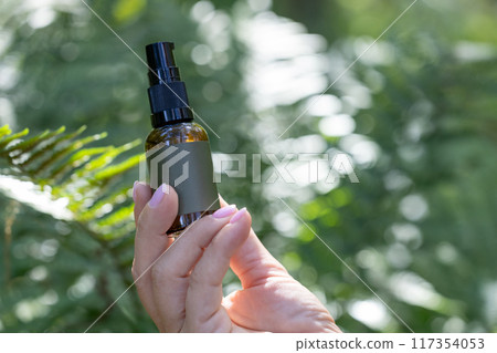 Spray Bottle Held in Hand with Green Foliage Background 117354053