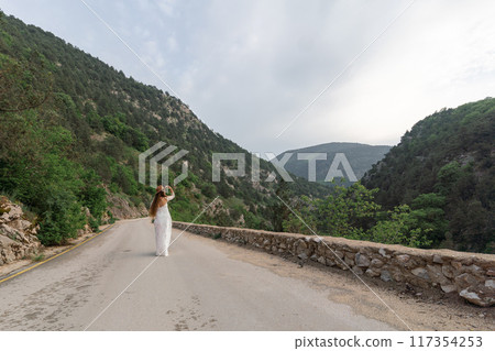 A woman is walking down a road in the mountains A woman is walking down a road in the mountains 117354253