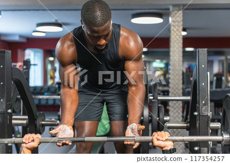Black fitness trainer helping another man at the gym with the barbell Black fitness trainer helping another man at the gym with the barbell 117354257