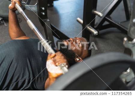 Concentrated black man lifting the barbell in bench press 117354265