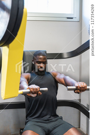 Black man working out hard on a gym machine Black man working out hard on a gym machine 117354269